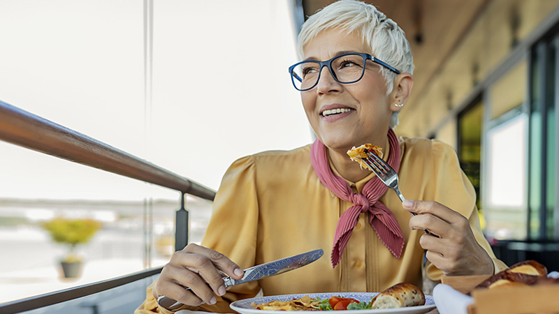 A senior woman is smiling while eating a balanced meal.