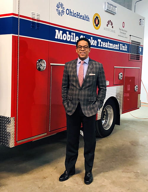 Dr. William Hicks is smiling while standing next to a Mobile Stroke Treatment Unit ambulance