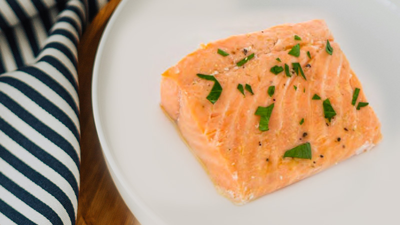 a salmon fillet sprinkled with green herbs is on a white plate