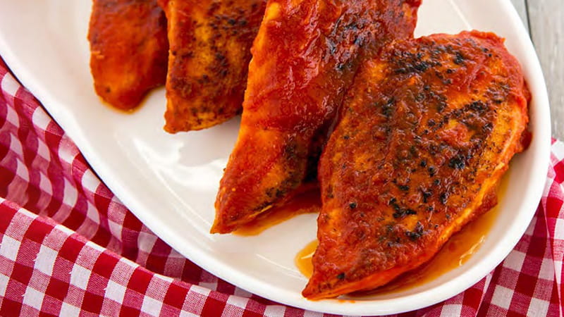 A platter of barbecued chicken breasts is on a red gingham tablecloth.
