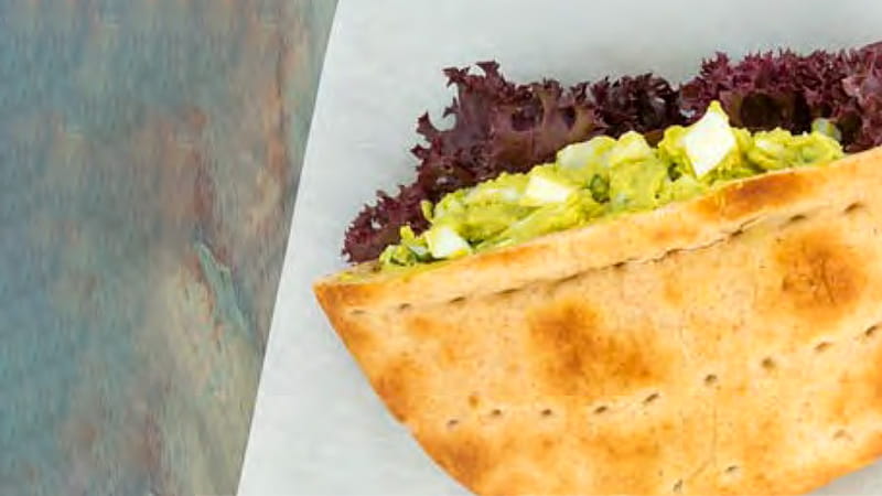 A pita pocket filled with egg avocado salad and lettuce is arranged on a plate.