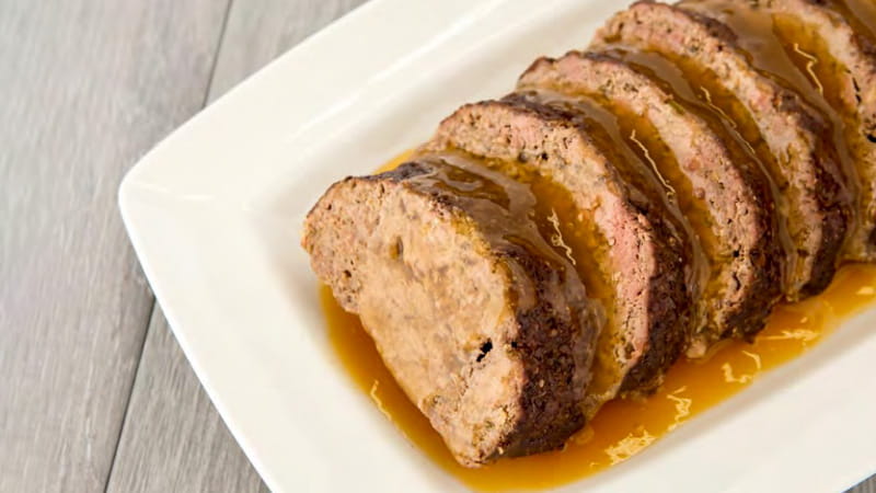 Slices of mushroom meat loaf in a sauce are neatly arranged on a platter.