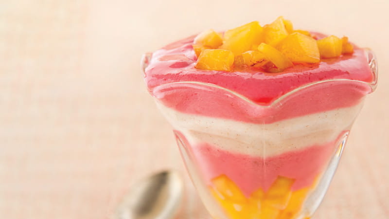 a parfait glass containing pink, white and yellow layers of yogurt and fruit