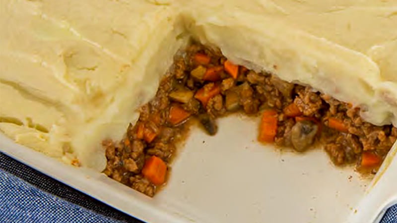 A Shepherd's Pie is in a casserole dish with a serving cut out showing the layers of meat and pastry top.