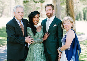 Steve, Dhivya, Danny and Deb are posing for a family wedding photo in an outdoor setting.
