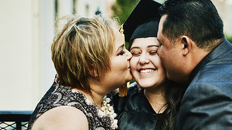 Madre y padre latinos besando a su hija graduada en una celebración familiar Madre y padre latinos besando a su hija graduada en una celebración familiar