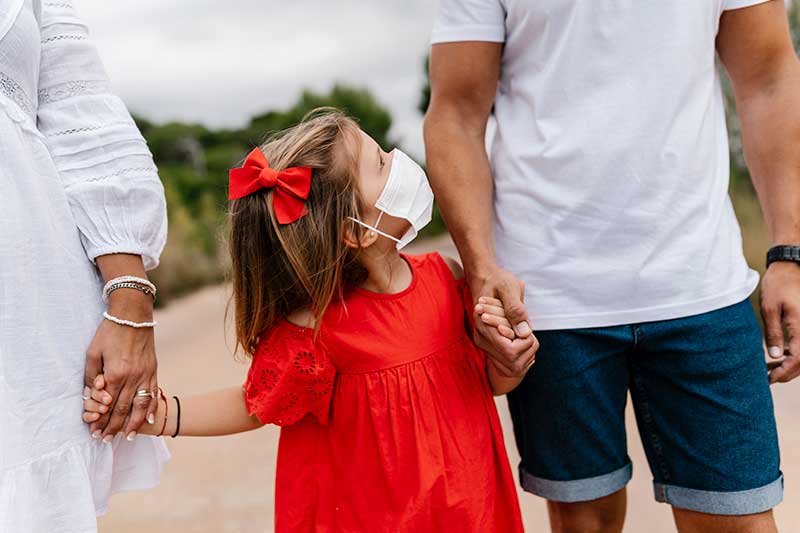 Familia tomándose de las manos, caminando con máscaras