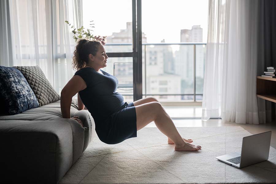 Mujer haciendo ejercicio en casa, apoyándose en el sofá