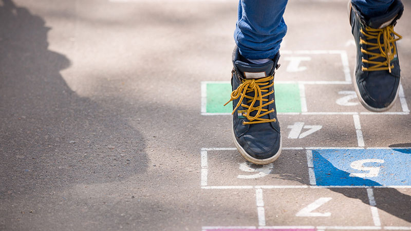 Primer plano de unos pies de niño jugando a la rayuela al aire libre