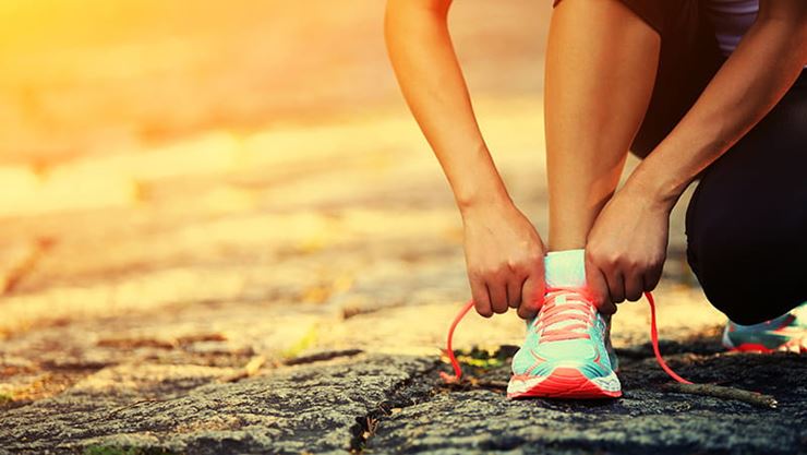 Mujer atándose los cordones de su calzado deportivo al aire libre durante el amanecer o el atardecer