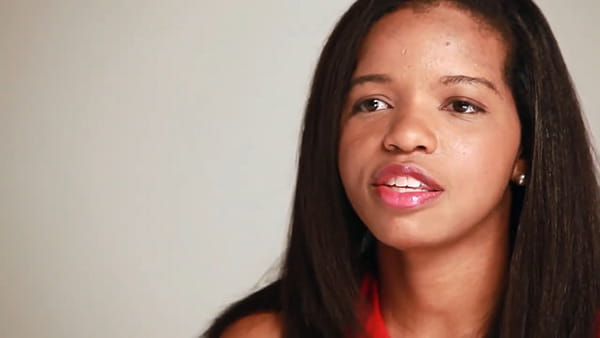 A video screen shot of stroke survivor, Tia, a young Black woman in front of a neutral background
