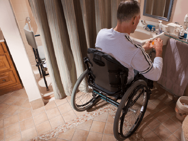 A man in a wheelchair is at the sink in his bathroom.