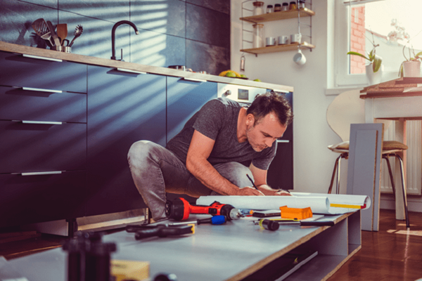 A casually-dressed man is constructing a cabinet in a kitchen.