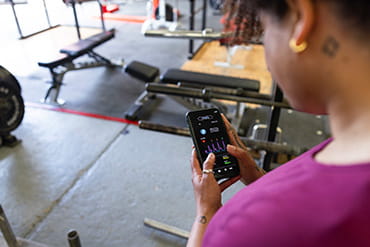 A person in a gym is looking down at their smartphone using a technology app to aid in their workout.