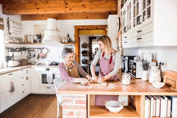 An older woman is kneading dough in a kitchen with family member.